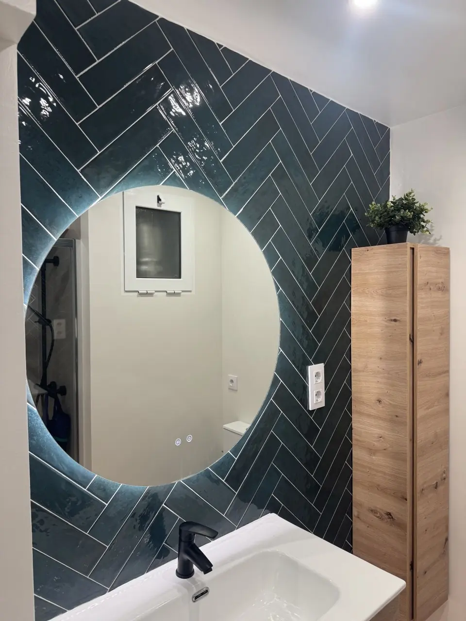Baño reformado con azulejo verde, espejo circular y mueble de madera