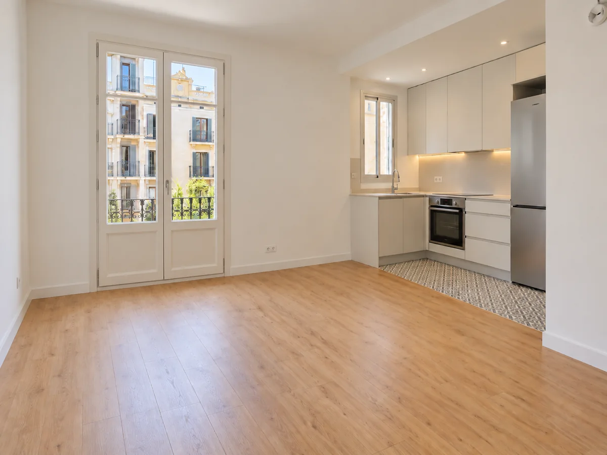 Salón de un piso reformado con cocina abierta, suelo de madera y balcón